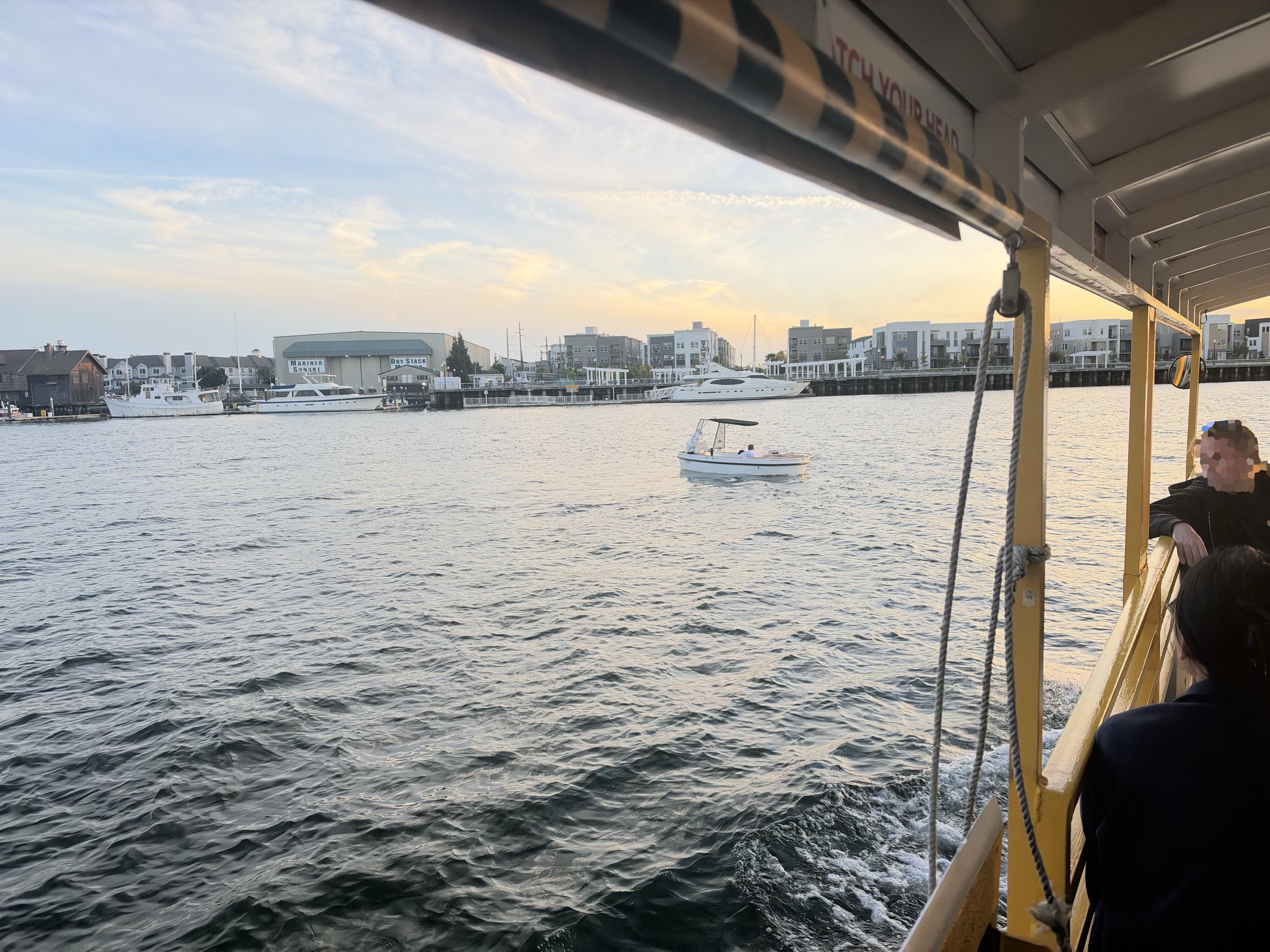 A view across the Oakland estuary towards Alameda from the estuary shuttle of a hot tub boat motoring along.